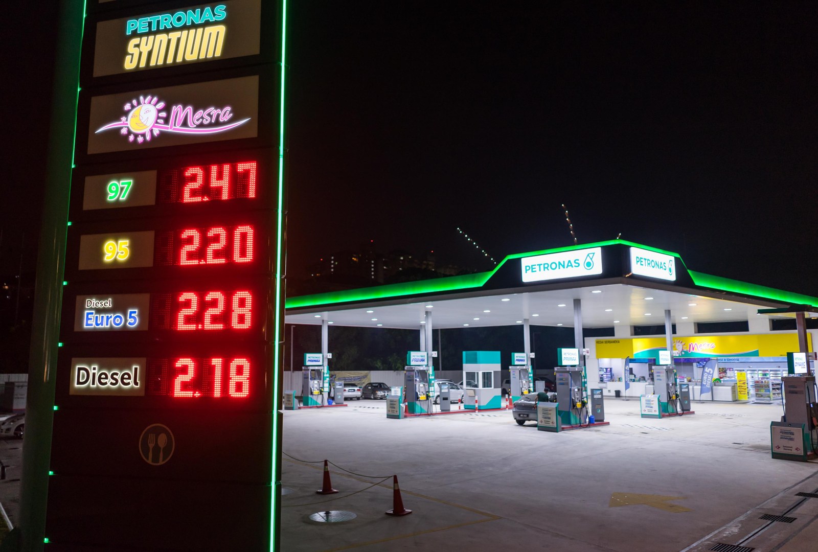 Petronas station at night — pylon digits and brand lightboxes both lit